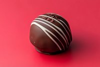 Dark chocolate truffle with white stripe decoration on vibrant red background, gourmet confectionery concept for food blogs and packaging.