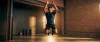 Fit male athlete performing explosive jump training in modern gym with brick walls and warm lighting for fitness and workout content.