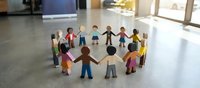 Diverse paper cutout people holding hands in circle representing unity, teamwork, community support, inclusion and collaboration in bright indoor space.