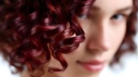 Young Caucasian woman with burgundy red curly hair and gentle smile in soft focus portrait composition, beauty and fashion concept for hair styling and coloring services.