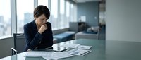 Professional Asian businesswoman analyzing financial documents at modern office desk with city view background for corporate presentations.
