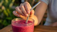 Woman's hand holding metal straw in vibrant berry smoothie drink outdoors. Fresh summer beverage with sustainable reusable straw for eco-friendly drinking.
