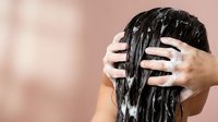 Woman applying hair mask treatment with hands massaging wet dark hair in bathroom for healthy haircare routine and scalp nourishment.