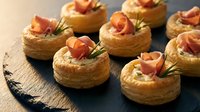 Elegant puff pastry appetizers topped with smoked salmon and fresh herbs on slate board for gourmet catering and fine dining presentations.