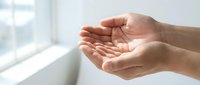 Open cupped hands in gentle receiving gesture against soft window light background for wellness meditation and spiritual concepts.