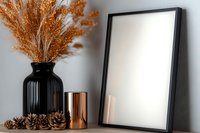 Minimalist home decor with black frame mockup, dried pampas grass in black ribbed vase, copper candle holder and pine cones on shelf against gray wall.