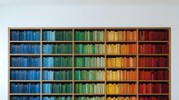 Large wooden bookshelf with books arranged by color creating rainbow gradient from blue to red, organized library wall display for interior design.