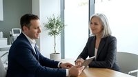 Professional business meeting between mature Caucasian woman and middle-aged Caucasian man in modern office discussing partnership agreement.