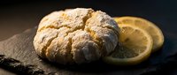 Freshly baked artisan bread loaf with golden crust on rustic slate board with lemon slices, warm lighting creates cozy bakery atmosphere for food photography.