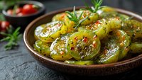 Marinated green tomatoes with herbs and spices in rustic bowl, homemade pickled vegetables for Mediterranean cuisine and healthy eating appetizer.