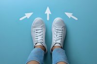 White sneakers and jeans viewed from above with three directional arrows pointing forward on turquoise background, representing choices, decisions and moving ahead.