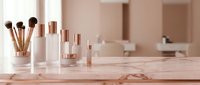Elegant skincare cosmetic bottles and makeup brushes arranged on marble surface in soft pink bathroom interior for beauty routine and self-care rituals.