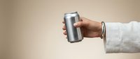 Hand holding blank silver aluminum beverage can against neutral beige background for mockup design and branding purposes.