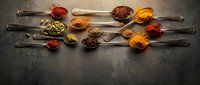 Colorful spices and seasonings arranged in vintage wooden spoons on dark rustic background for culinary cooking and food preparation concepts.
