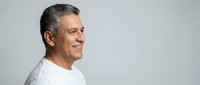 Smiling mature Hispanic man in white shirt looking away with confident expression against gray background for business and lifestyle concepts.