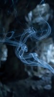 Delicate blue smoke swirls gracefully against a dark moody background, creating an ethereal and mysterious atmosphere for creative projects.