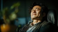 Middle-aged Asian man relaxing with eyes closed in comfortable chair, peaceful expression showing stress relief and meditation at home interior.