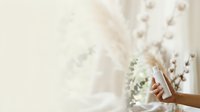 Closeup of female hand holding wooden stick near white dried flowers and eucalyptus branches for home decor, wellness, and interior design projects.