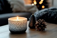 Cozy winter home decor with burning candle in decorative holder and pine cone on wooden table creating warm atmospheric lighting for relaxation and comfort.