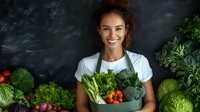 Young mixed race female chef in green apron holding fresh organic vegetables and greens in metal container against dark background, promoting healthy eating and farm to table concept.
