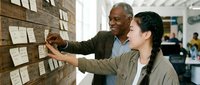 Senior African American businessman mentoring young Asian female colleague at office planning board during strategic meeting.