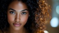 Young African American woman with natural curly hair and glowing skin smiling softly at camera against blurred background, beauty and fashion portrait.