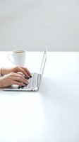 Hands typing on laptop computer with coffee cup on white desk in minimalist workspace for remote work and productivity.