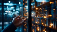 Hand touching glass door with condensation against blurred city lights at night, creating atmospheric mood with bokeh effect.