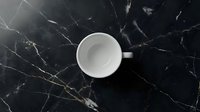 Empty white ceramic cup on black marble surface with gold veining, overhead view. Suitable for beverage, kitchen, and lifestyle design projects.
