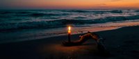 Romantic beach sunset with candle creating warm ambiance on sandy shore. Ocean waves and golden sky provide serene backdrop for intimate evening moments.