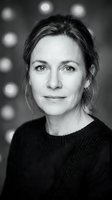 Black and white portrait of a confident Caucasian middle-aged woman in a knit sweater, with bokeh lights in the background.
