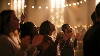 Diverse group of people worshipping together in a warmly lit church, hands raised in prayer and praise during a spiritual gathering.
