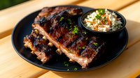 Grilled pork ribs with caramelized glaze served on black plate with fresh coleslaw side dish, garnished with chopped herbs on wooden table surface.