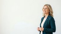 Middle-aged Caucasian woman in professional business attire wearing dark teal blazer over white shirt, smiling confidently while looking upward. Suitable for corporate, leadership, and business concepts.