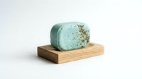 Handmade teal herbal soap bar with dried herbs on a wooden soap dish, isolated on white background for natural skincare and organic beauty product use.