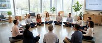 Diverse group practicing mindfulness meditation in modern office space with natural light for workplace wellness and stress reduction programs.