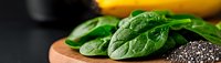 Fresh raw spinach leaves and chia seeds on wooden cutting board against dark background, healthy superfood ingredients for nutritious meal preparation.
