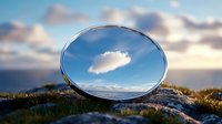 Circular mirror on rocky coastal terrain reflecting single cloud in blue sky, creating optical illusion against blurred sunset background.