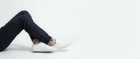 Legs in dark blue jeans and white leather sneakers on a light background, casual street style fashion concept for lifestyle and apparel design.