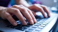 Professional hands typing on modern laptop keyboard in office environment with soft lighting and technology workspace background.