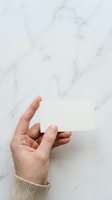 Hand holding blank white business card against marble background, ideal for branding mockups and corporate identity presentations.
