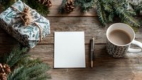 Festive Christmas flatlay with wrapped gift, blank card, coffee mug, pine branches and pinecones on rustic wooden table. Holiday planning scene.