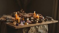 Mystical altar with glowing candles, singing bowls, crystals, and sage smudge sticks on a rustic wooden table for spiritual rituals.
