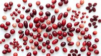 Mixed red berries and fruits scattered on white background including cranberries blueberries cherries and dried fruits for healthy eating concepts.