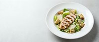 Grilled chicken breast sliced and served with fresh Caesar salad, croutons, and parmesan on white plate for restaurant menu or food blog.