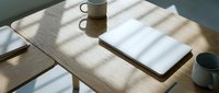 Wooden desk with sunlight casting shadows, featuring blank notebook, ceramic mug, and minimalist workspace setup for creative projects and office design concepts.