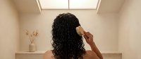 Woman with curly hair relaxing in modern bathtub under skylight in minimalist bathroom interior for wellness and self-care concepts.