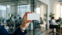 Businessman holding blank white business card in modern office environment with colleagues working in background.