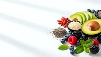 Superfood ingredients with fresh berries, avocado, quinoa and chia seeds arranged on white marble surface for healthy nutrition and wellness lifestyle.
