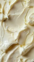Creamy white frosting texture with soft swirls and peaks, macro photography showing rich, smooth surface detail and tiny air bubbles in dairy dessert topping.